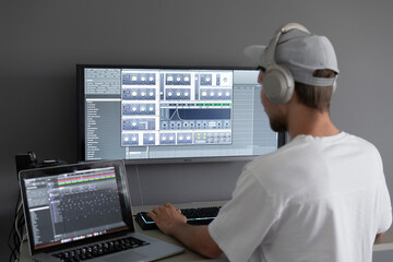 male producer in headphones doing music at home using computer