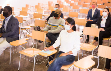 Wall Mural - Group of diverse business people wearing face masks for viral protection and keeping social distance listening to speaker at conference, the new normal