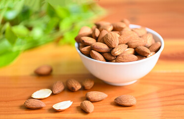 Wall Mural - Almonds nuts on white bowl and green leaf on background, Delicious sweet almonds on the wooden table , roasted almond nut for healthy food and snack