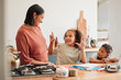 © Kay Abrahams/peopleimages.com - A mother smiling, teaching and helping children with homework in the kitchen. Mom and kids using the internet to homeschool her young daughter and son, to help with math, for a happy family and kids.