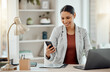 © C Coetzee/peopleimages.com - Freelance and remote working business woman checking her phone, reading a message or sending a text in her home office. Motivated, happy and positive female professional sitting at her desk at work