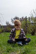 © Anna - Happy redhead boy playing tablet or watching cartoons while sitting on green grass in the backyard in the village, vacation