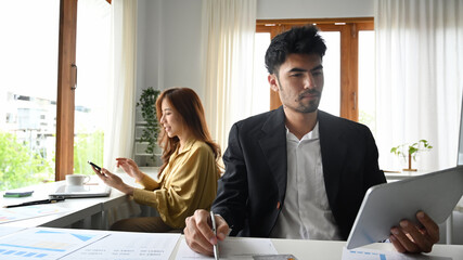 Wall Mural - Millennial male manager checking financial reports and using digital tablet on white office desk