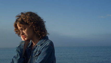 Wall Mural - Sad woman standing on sea beach. Portrait of upset girl holding hand on face