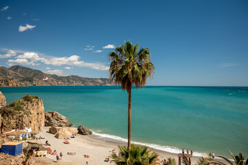 Travel destination, view on sandy beach, blue sea and mountains from Balcon de Europa in small Andalusian town Nerja with white houses and narrow streets on Costa del Sol, Spain