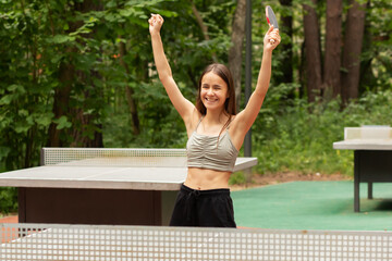 Wall Mural - ping pong winner, happy girl with a racket raised her hands up, rejoices at the victory, sports success