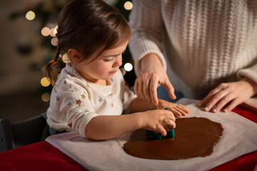 Poster - family, cooking and winter holidays concept - happy mother and baby daughter with mold making gingerbread cookies from dough at home on christmas