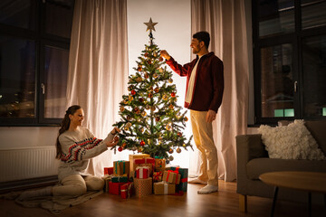 winter holidays and people concept - happy couple decorating christmas tree at home