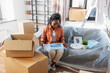 © Syda Productions - moving, people and real estate concept - happy smiling woman packing boxes sitting on sofa at home