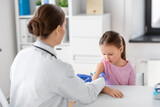 Fototapeta  - medicine, healthcare and vaccination concept - female doctor or pediatrician with syringe making vaccine injection to little girl patient at clinic