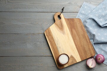 Cutting board, onion and salt on grey wooden table, flat lay with space for text. Cooking utensil