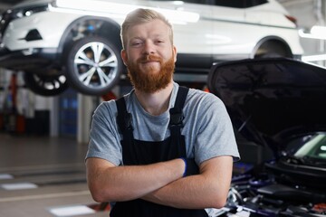 Portrait of a successful car mechanic in a clean uniform against the background of a car on a lift at a service station