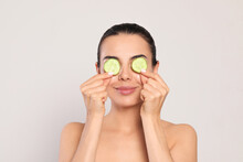 Beautiful Young Woman Putting Slices Of Cucumber On Eyes Against Light Grey Background