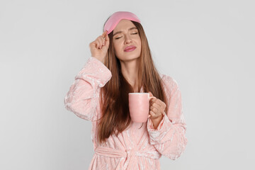 Sticker - Beautiful young woman in bathrobe with cup of coffee on light background