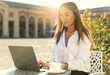 © Paulista - Young attractive woman using laptop and sitting in an outdoor cafe. Remote working or studying concept.