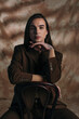 © LIGHTFIELD STUDIOS - Queer person in jacket looking at camera while sitting on chair on abstract brown background.
