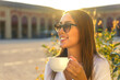 © Paulista - Head shot of smiling young woman in sunglasses having a cup of cappuccino outside.