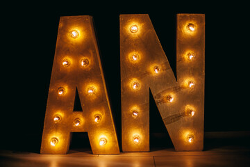 Wall Mural - AN letters close-up. Letters for the sign with the bulbs. Letters AN on a yellow light bulb and a black background. Loft idea. Lamps on a wooden stand. Letters AN in interior. Soft focus