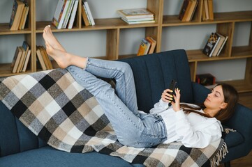 Close up of a relaxed girl using a smart phone lying on a sofa in the living room at home.