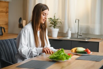 Wall Mural - Beautiful young woman is preparing vegetable salad in the kitchen. Healthy Food. Vegan Salad. Diet. Dieting Concept. Healthy Lifestyle. Cooking At Home.