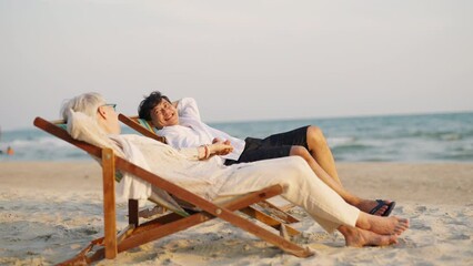 Wall Mural - Happy Asian family senior couple enjoy outdoor lifestyle on summer beach holiday vacation at the sea. Elderly retired man and woman relaxing on beach chair and holding hands together at summer sunset