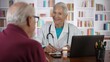 © Robert Peak - Mature senior female doctor talking to male patient in modern clinic with library background.