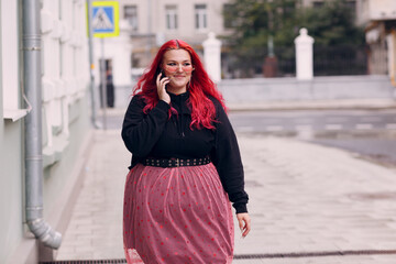 Wall Mural - European plus size woman use mobile phone outdoor. Young red pink haired body positive girl walk at city street outdoors