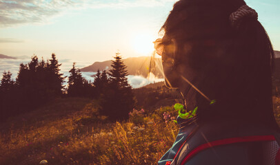 Wall Mural - Young fit happy woman stand on viewpoint after reach top in mountains. Carefree tourist woman looking at sun enjoying landscape. Girl traveler on top of mountain in rays of sunset