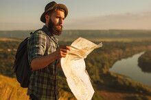 Male Hiker Reading Map And Admiring Scenic River Flowing In Countryside