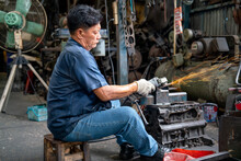 Asian Senior Mechanic Use Machine To Lathe Metal Autoparts Occur Sparks And He Work In Garage Workplace.