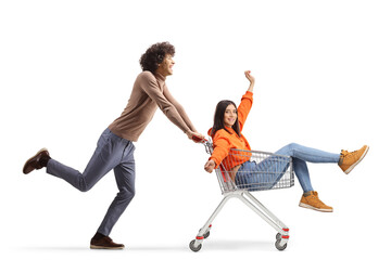 Poster - Full length profile shot of a young man running and pushing a girl inside a shopping cart