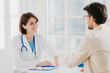 © VK Studio - Friendly female doctor greets patient with handshake, pose in private clinic, sit opposite each other, have talk, agree to sign insurance contract, meet in hospital. Health care and medicine concept