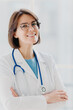 © VK Studio - Close up portrait of short haired female general practitioner stands with smile and arms crossed, uses stethoscope, enjoys work, poses against white background. People, mediccare and treatment concept