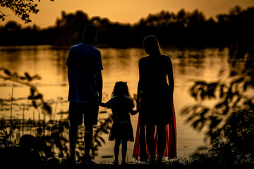 silhouette of a family watching the sunset on the shore of a lake