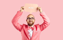 Smiling Young Man In Suit On Pink Studio Background Hold Speech Bubble With Dots. Happy Funny Male In Jacket Show Balloon Or Banner For Online Communication. Messenger App Concept.