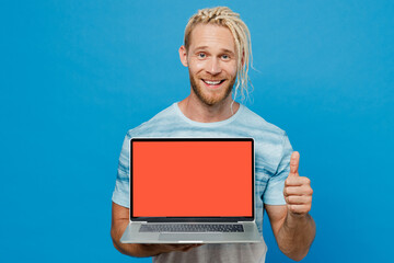 Young happy fun blond man with dreadlocks 20s he wear white t-shirt hold use work on laptop pc computer with blank screen workspace area show thumb up isolated on plain pastel light blue background