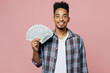 © ViDi Studio - Young smiling happy man of African American ethnicity 20s he wear blue shirt hold in hand fan of cash money in dollar banknotes isolated on plain pastel light pink background People lifestyle concept
