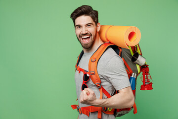 Side view young traveler white man carry backpack stuff mat show thumb up isolated on plain green background Tourist leads active lifestyle walk on spare time. Hiking trek rest travel trip concept