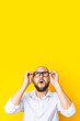 Bald young man holding glasses looks up itchy on a yellow background