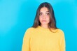 Stunned beautiful brunette woman wearing yellow sweater over blue background stares reacts on shocking news. Astonished woman holds breath