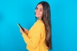 © Jihan - Rear view photo portrait of beautiful brunette woman wearing yellow sweater over blue background using smartphone smiling