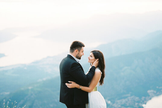 Groom hugs bride, holding her head in his hands against the backdrop of the Kotor Bay