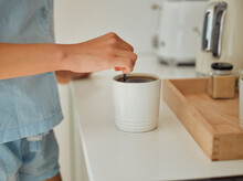 Making fresh, hot morning coffee indoors on a kitchen counter to start the day. Hand closeup of preparing a warm beverage and drink inside with a female standing in pajamas at home