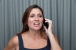 Angry middle aged 40+ or 50+ year old woman yelling into a cell phone with mad facial expression