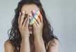 © illustrissima - Portrait of a young woman covering her eyes with her palms and laughing with the reflection of a rainbow on her hands. The girl closed her eyes and enjoys life. Emotional psychological state. lgbt sym