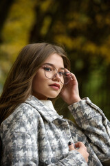 Poster - Close-up portrait of young woman in a stylish trench coat and in a white sweater resting on the bench. warm autumn day.