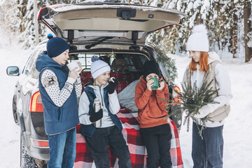 Wall Mural - Four friends teenagers boys and girl with thermos sitting in trunk of car decorated for Christmas and New year. Winter picnic in snowy forest. Road trip and local travel. Friends hanging out together