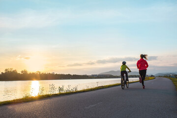 Happy mother and son go in sports outdoors. Boy rides bike in helmets, mom runs on sunny day. Silhouette family at sunset. Fresh air. Health care, authenticity, sense of balance and calmness	