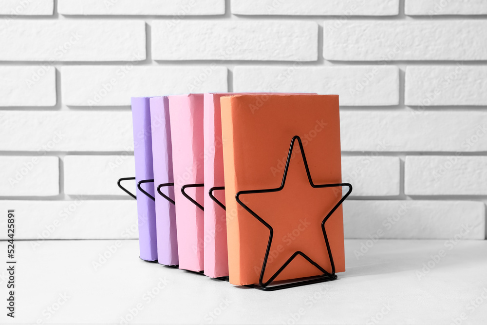 Metal holder with books on table near white brick wall
