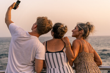 beautiful mother with her two twenty year old sons take a selfie by the sea at sunset